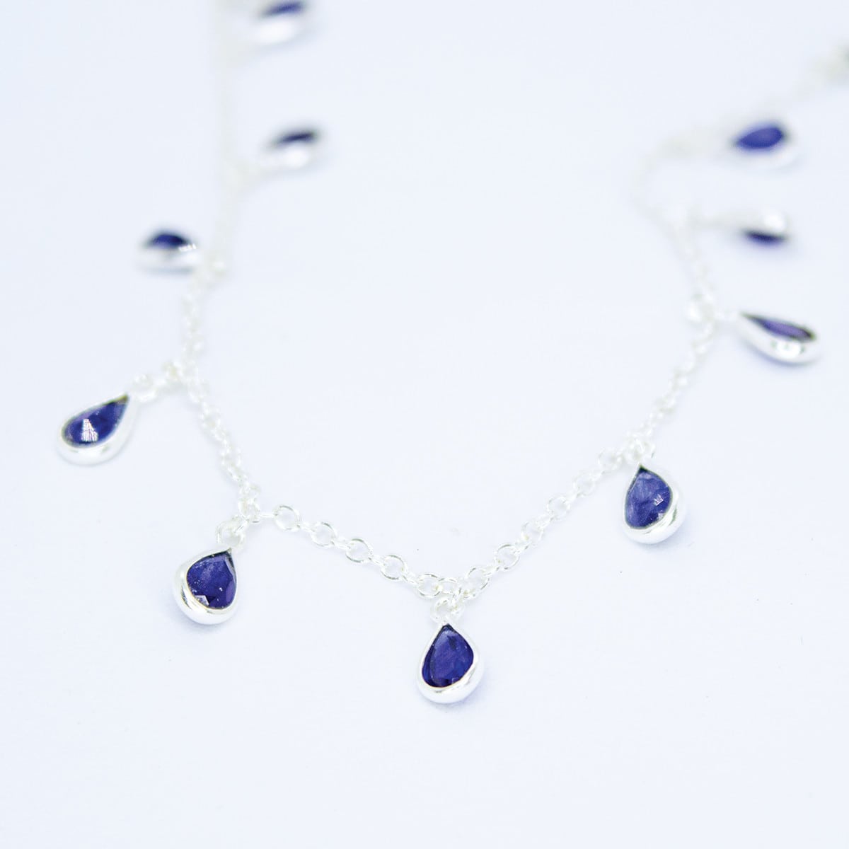 Flat lay view of Sterling Silver necklace with eighteen 5 x 3mm pear-shaped Sapphire gemstones on 42cm chain, 5cm extension.