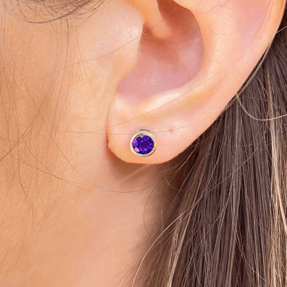 Close-up front view of a woman wearing the Amethyst Tube Set Studs, highlighting a 5mm round Amethyst gemstone set in sterling silver tube setting.