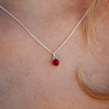 Close-up front view of woman wearing the Garnet Pendant around her neck. The necklace features a 5mm round Garnet gemstone set in four claws on a 45cm curb chain.