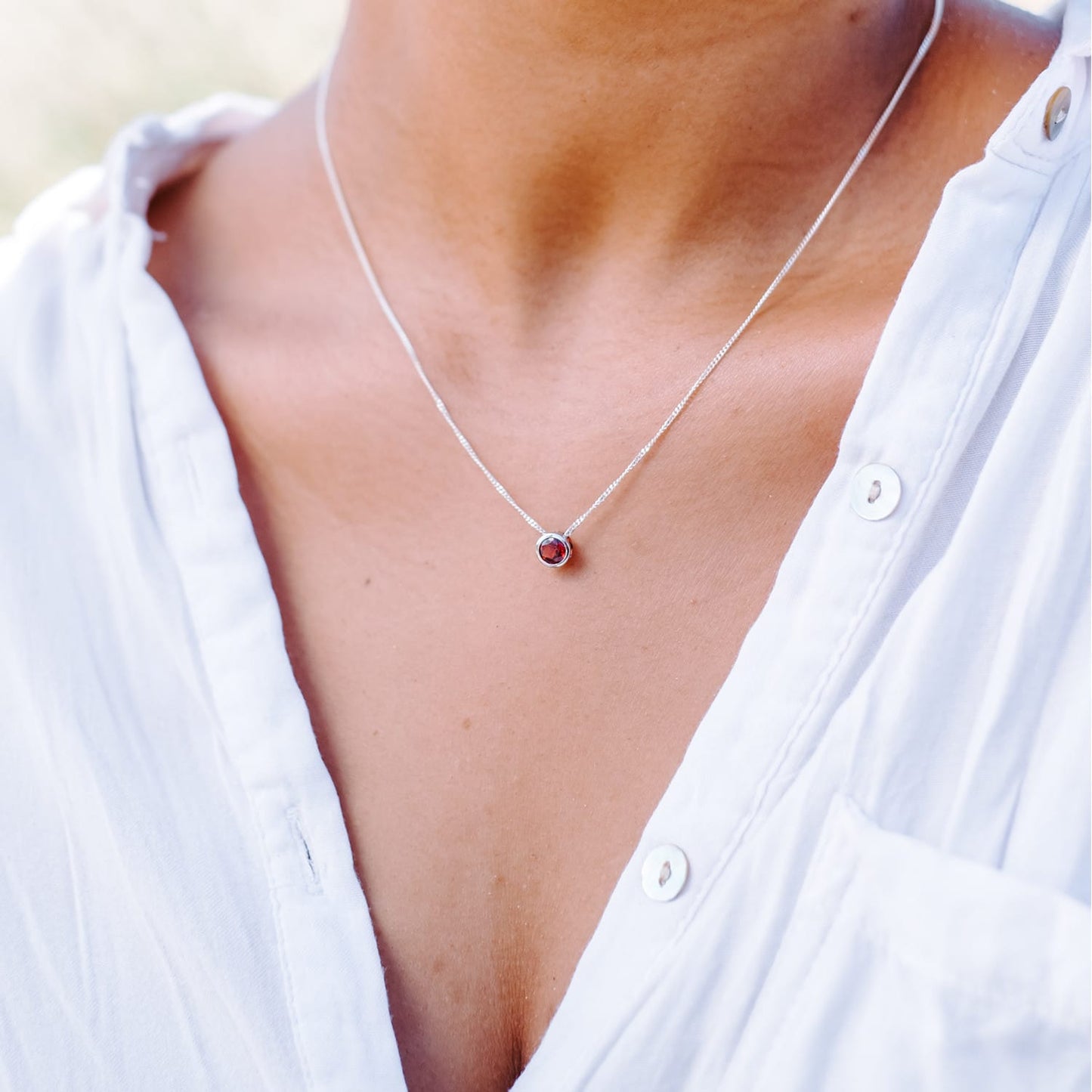 A woman wearing the Garnet Slider Necklace around her neck. The necklace features a 5mm Garnet gemstone set in a Sterling Silver tube setting on a 45cm long chain.