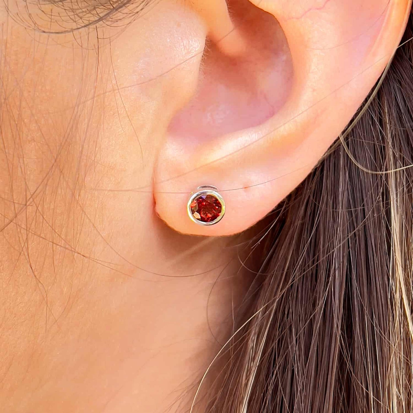 Frontal view of a woman wearing the Garnet Tube Set Stud earrings. The earrings feature a 5mm round Garnet gemstone set in a Sterling Silver tube setting.