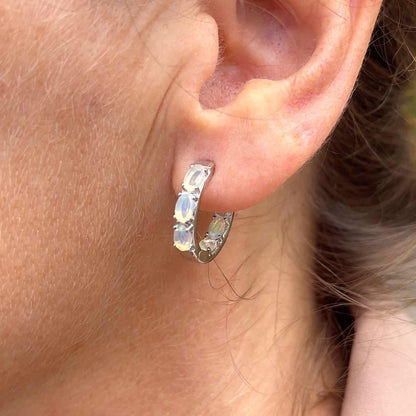 Slight side view of Ethiopian Opal Huggie earring on woman's ear. Features six oval 5 x 3mm Ethiopian Opal gems set in Sterling Silver huggie hoops.