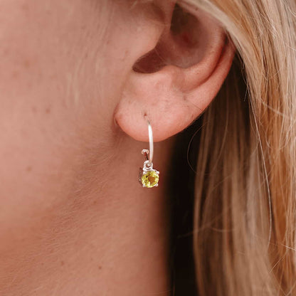 Side view of woman wearing Peridot Dangle Hoop earrings. Sterling Silver Hoop with 5mm round Peridot gemstone in four claws.