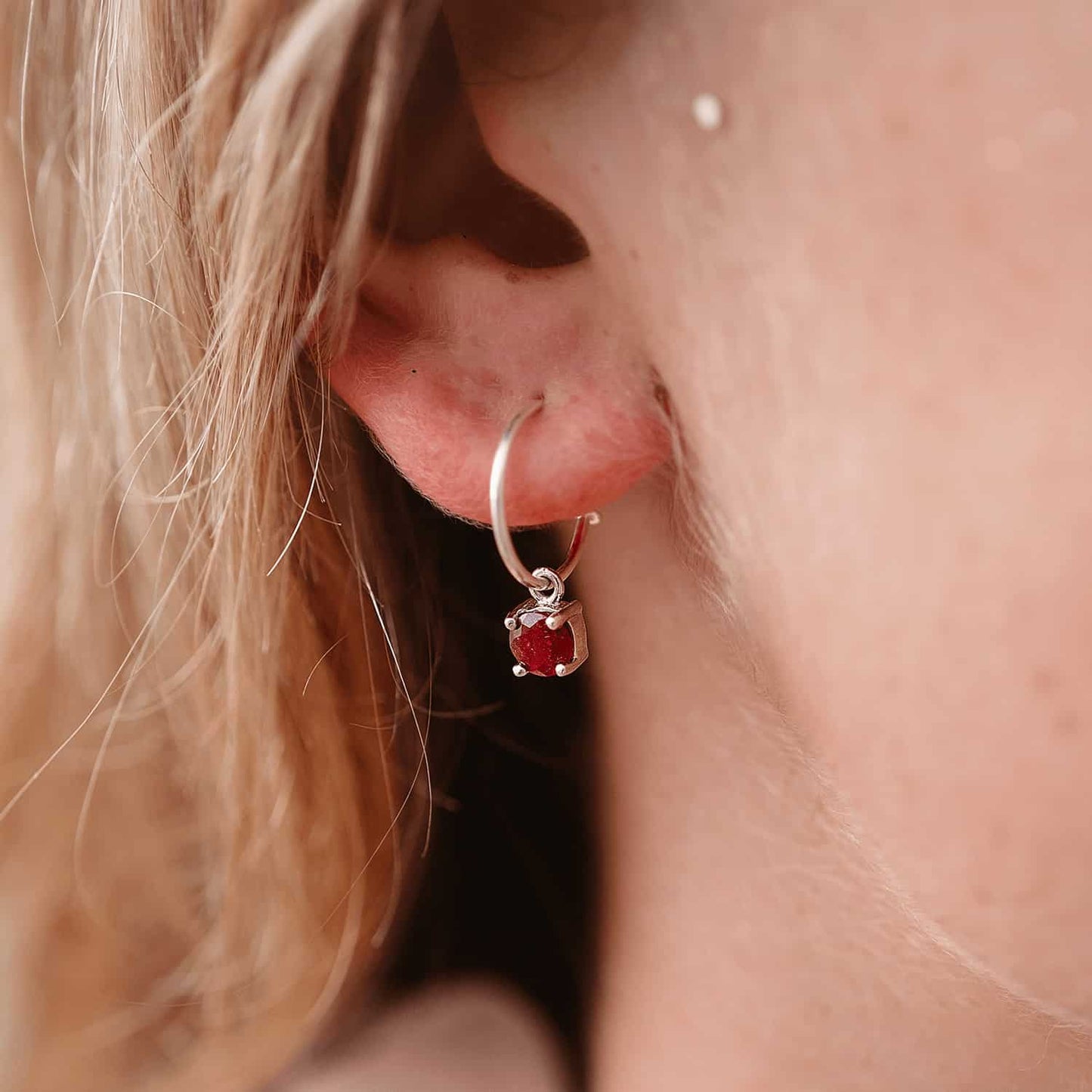 Side view image of a woman wearing Ruby Dangle Hoop earrings with detachable 5mm round Ruby gemstones set in four claws.