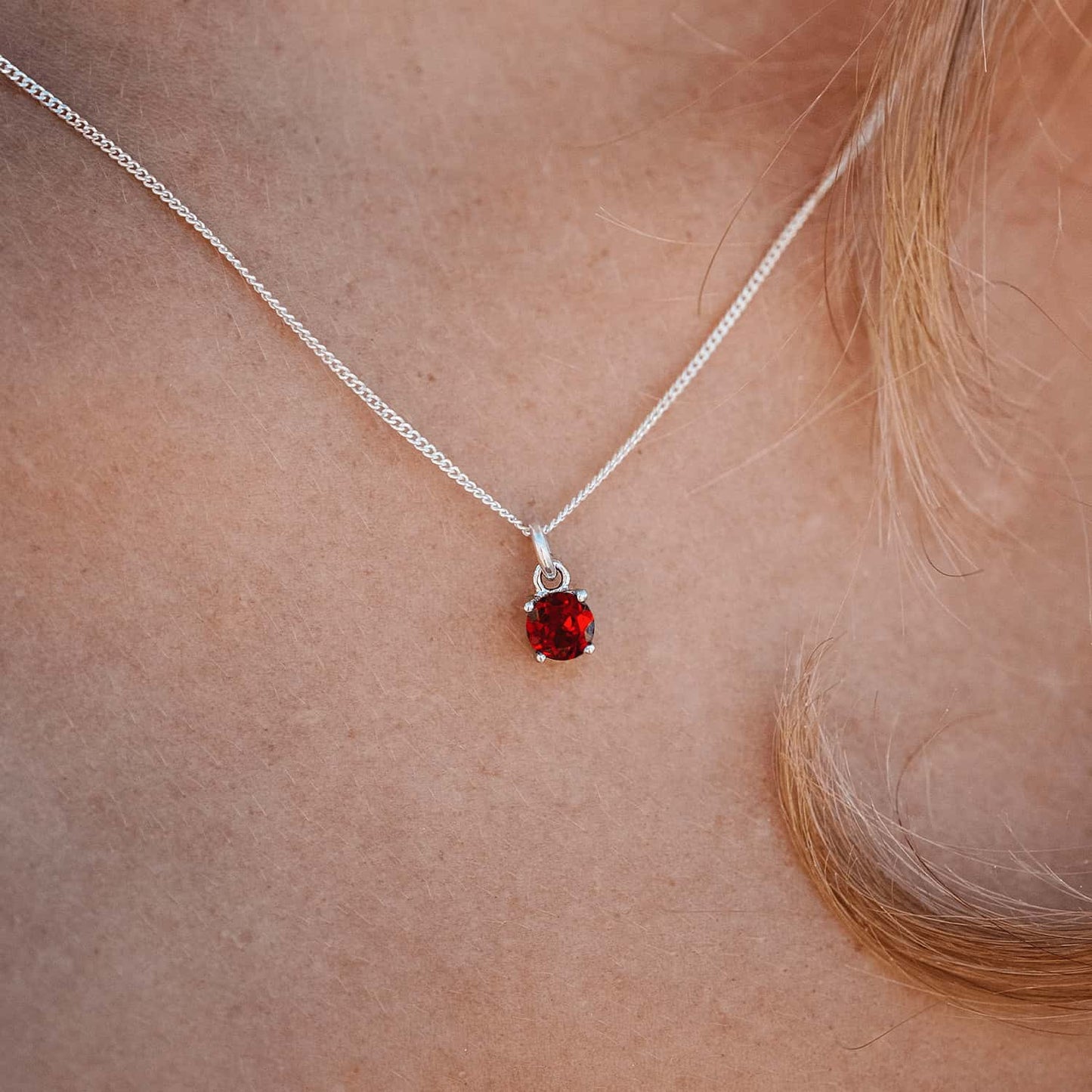 Woman wearing the Ruby Pendant necklace with a 5mm round Ruby gemstone set in four claws on a 45cm sterling silver curb chain.