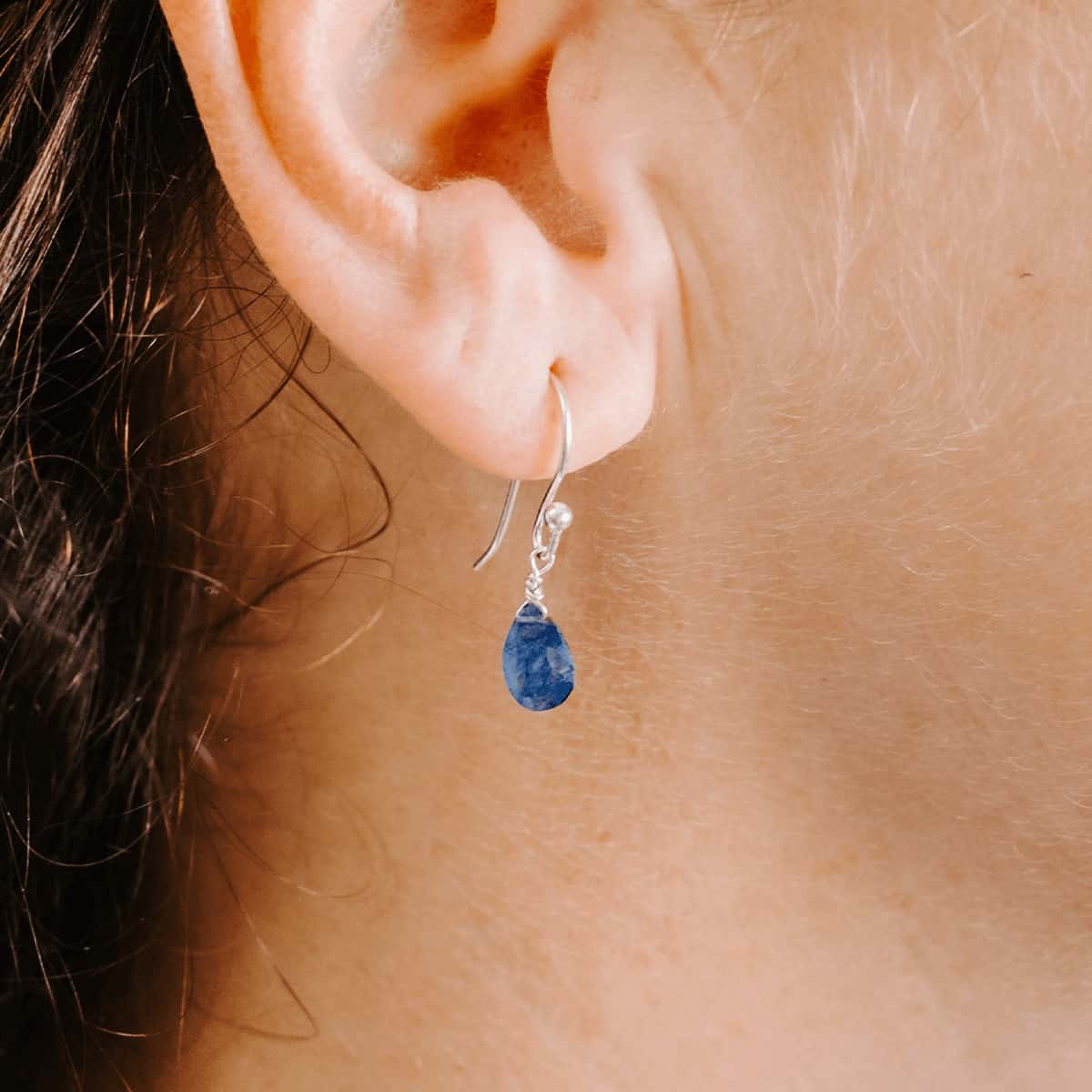 Close up front view of woman wearing Sterling Silver shepherd’s hook earring with Sapphire drop.