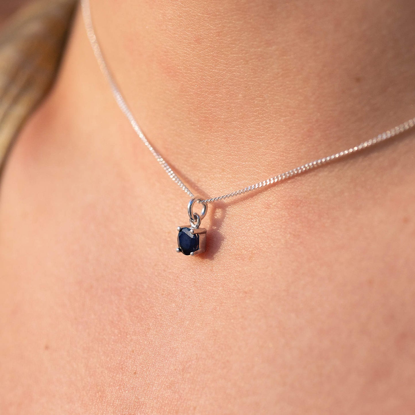 Woman wearing Sapphire Pendant necklace with 5mm round Sapphire gemstone on 45cm curb chain, viewed from the side.