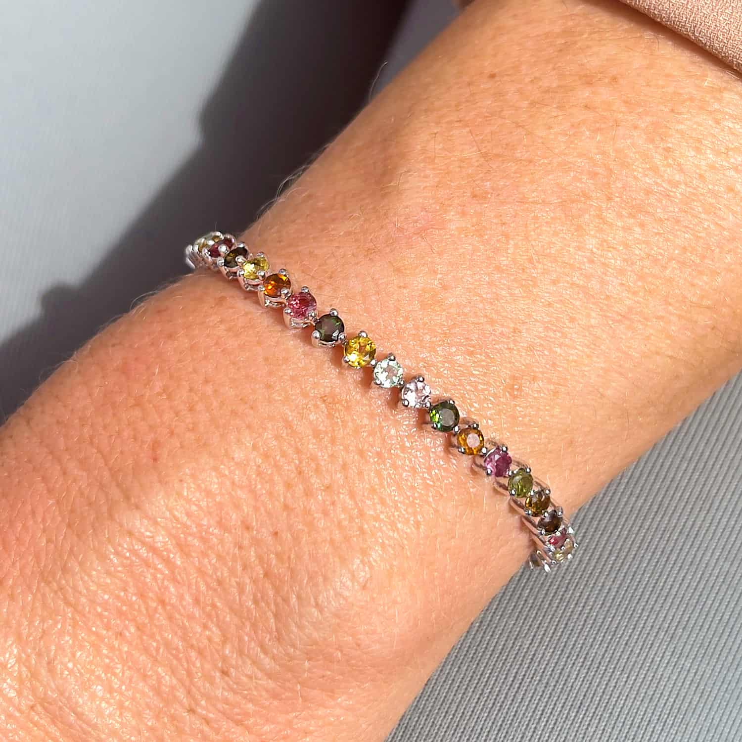 Sterling Silver Tennis Bracelet adorned with 30 Round Brilliant Cut Multicoloured Tourmaline gemstones, seen from above on a woman's wrist.