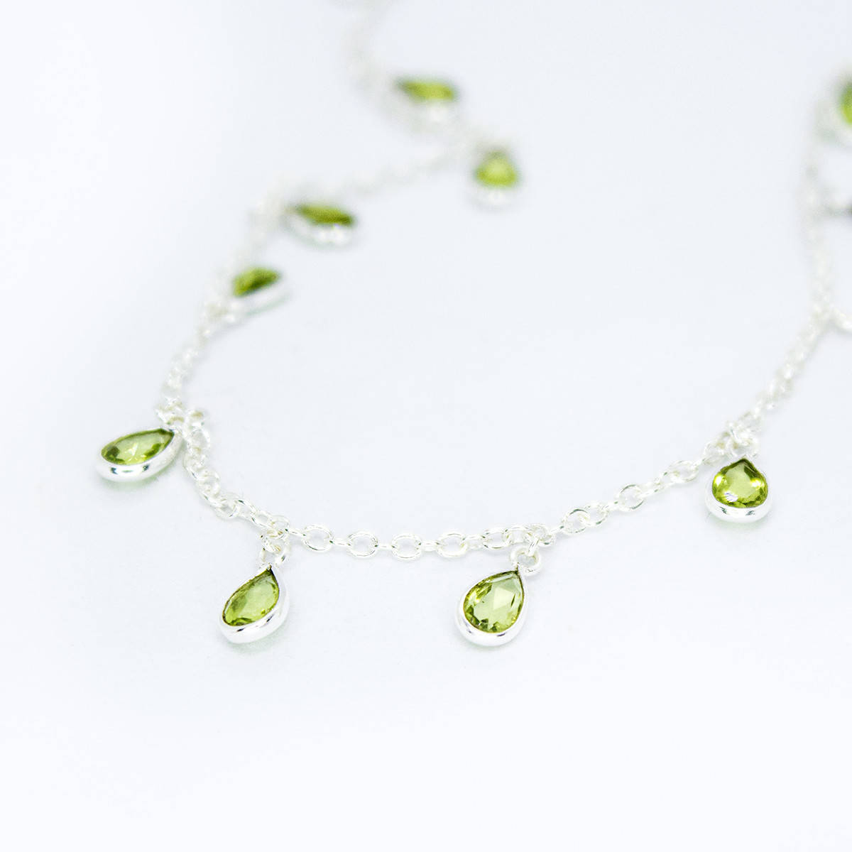 Flat lay view of Sterling Silver necklace with eighteen 5 x 3mm pear-shaped Peridot gemstones on 42cm chain, 5cm extension.