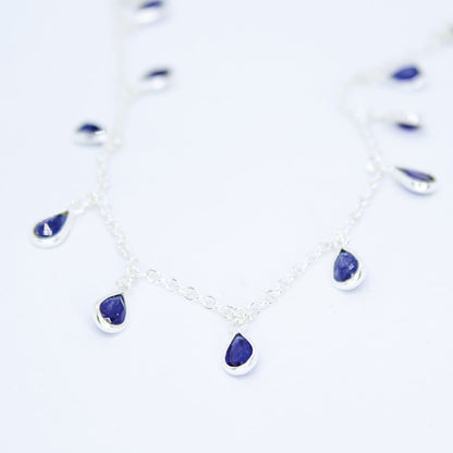 Flat lay view of Sterling Silver necklace with eighteen 5 x 3mm pear-shaped Sapphire gemstones on 42cm chain, 5cm extension.