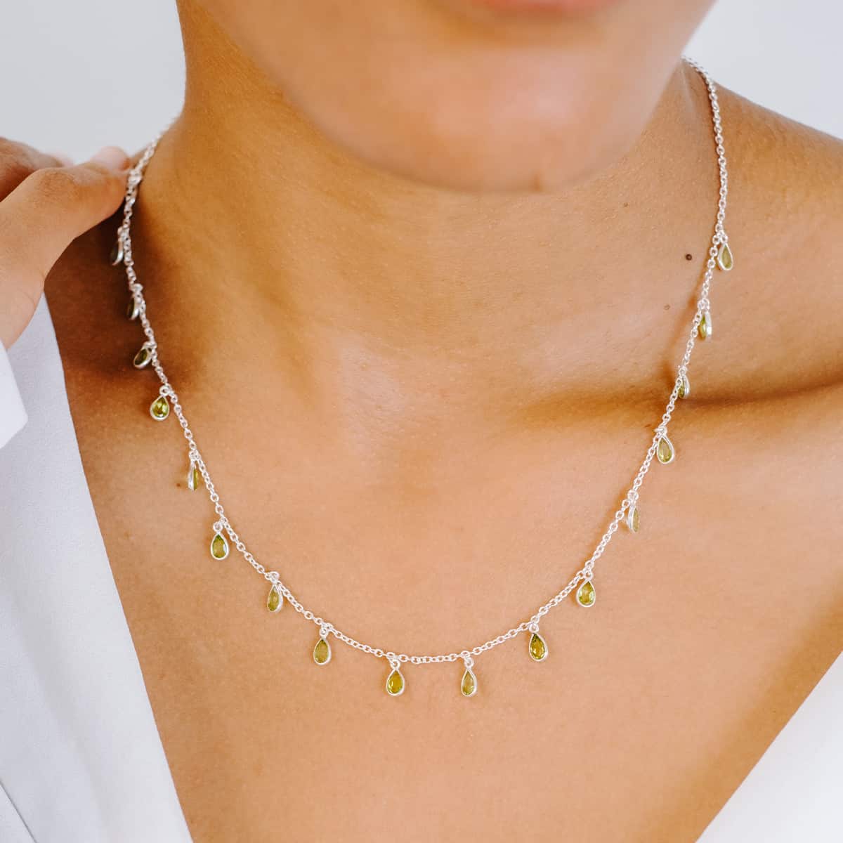 Front view of woman wearing Sterling Silver necklace with eighteen 5 x 3mm pear-shaped Peridot gemstones on 42cm chain.