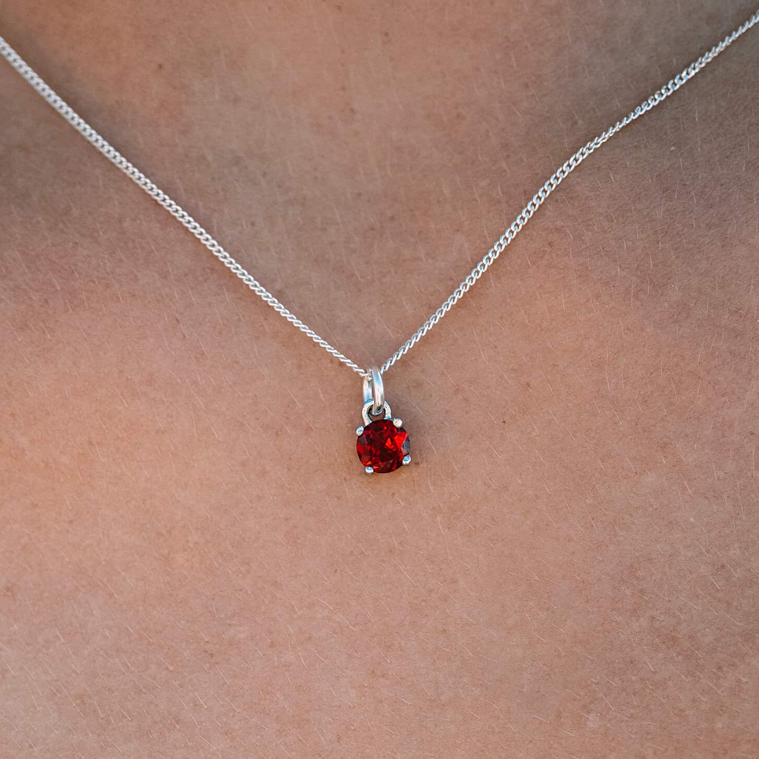 Close-up front view of woman wearing the Garnet Pendant necklace. The necklace features a 5mm round Garnet gemstone set in four claws on a 45cm curb chain.