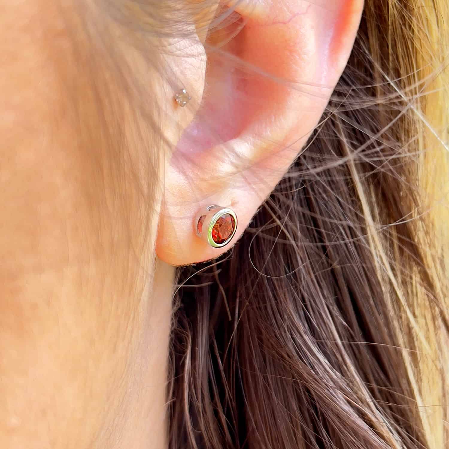 Side view of a woman wearing the Garnet Tube Set Stud earrings. The earrings feature a 5mm round Garnet gemstone set in a Sterling Silver tube setting.