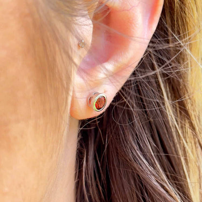 Side view of a woman wearing the Garnet Tube Set Stud earrings. The earrings feature a 5mm round Garnet gemstone set in a Sterling Silver tube setting.