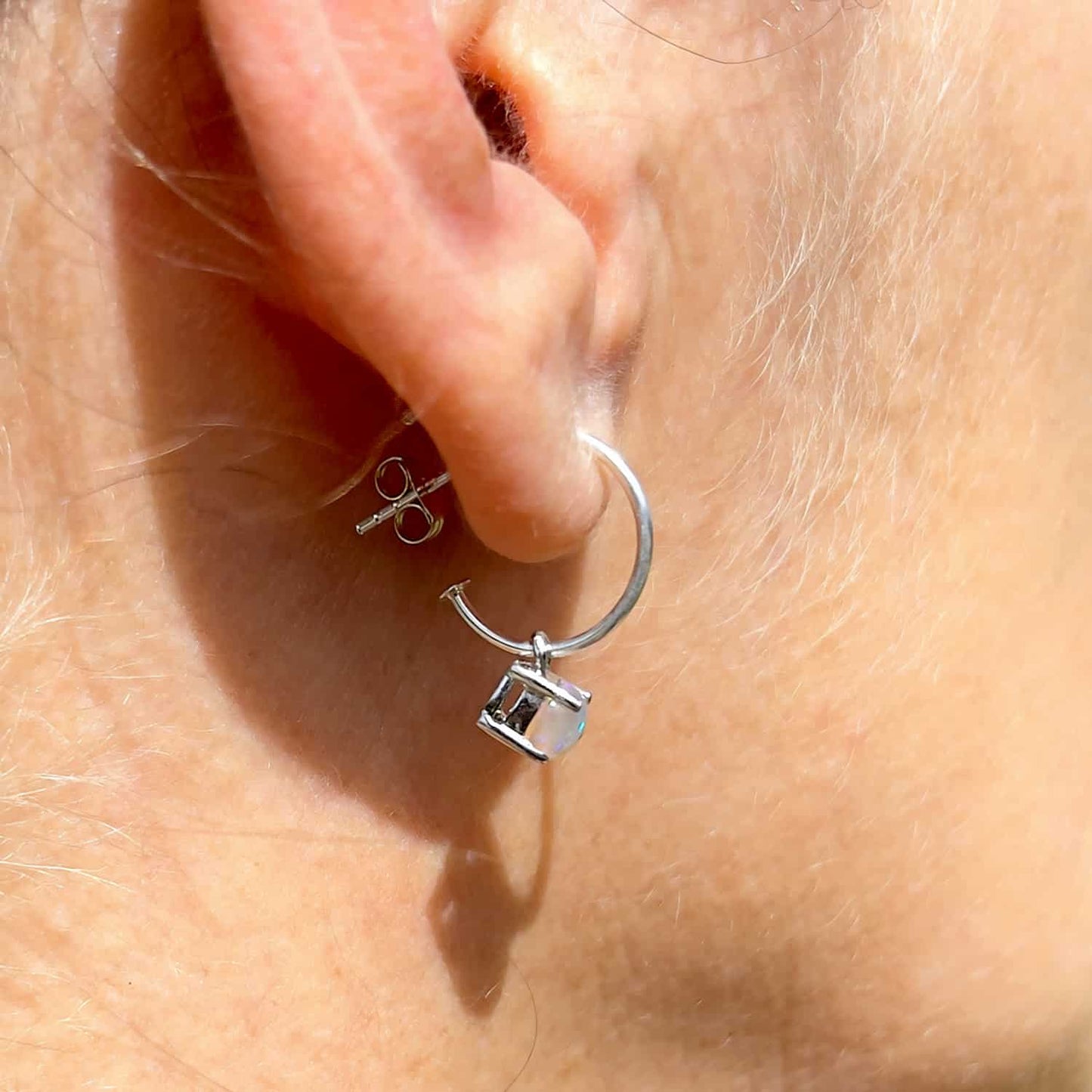 Side view of woman wearing Ethiopian Opal Dangle Hoop earring, showcasing stunning opal gemstone in Sterling Silver.