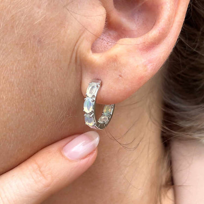 Woman's ear viewed from slight side, pointing at Ethiopian Opal Huggie earring. Features six oval 5 x 3mm Ethiopian Opal gems set in Sterling Silver huggie hoop.