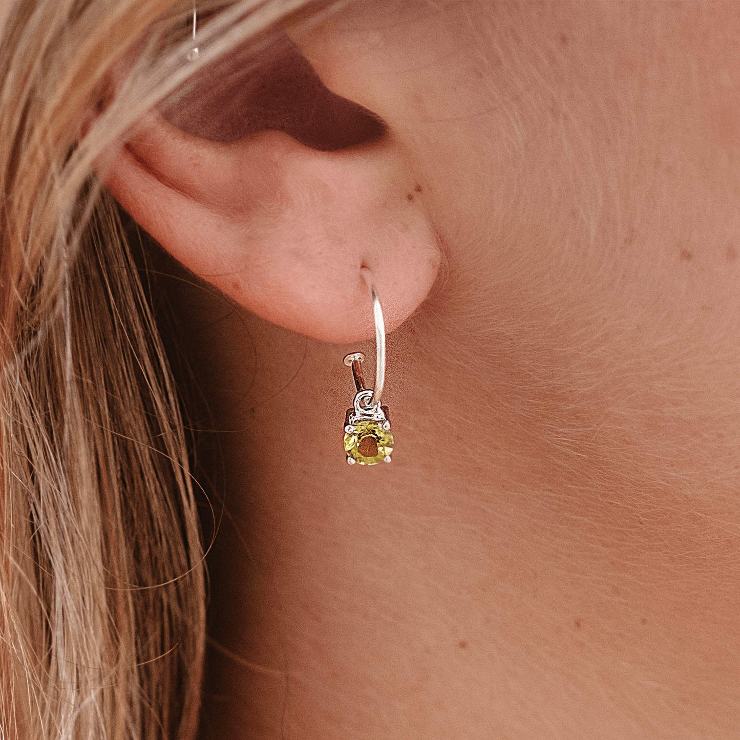 Front view of woman wearing Peridot Dangle Hoop earrings. Sterling Silver Hoop with 5mm round Peridot gemstone in four claws.