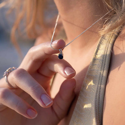 Woman holding Sapphire Pendant necklace with 5mm round Sapphire gemstone on 45cm curb chain, showcasing its exquisite design.