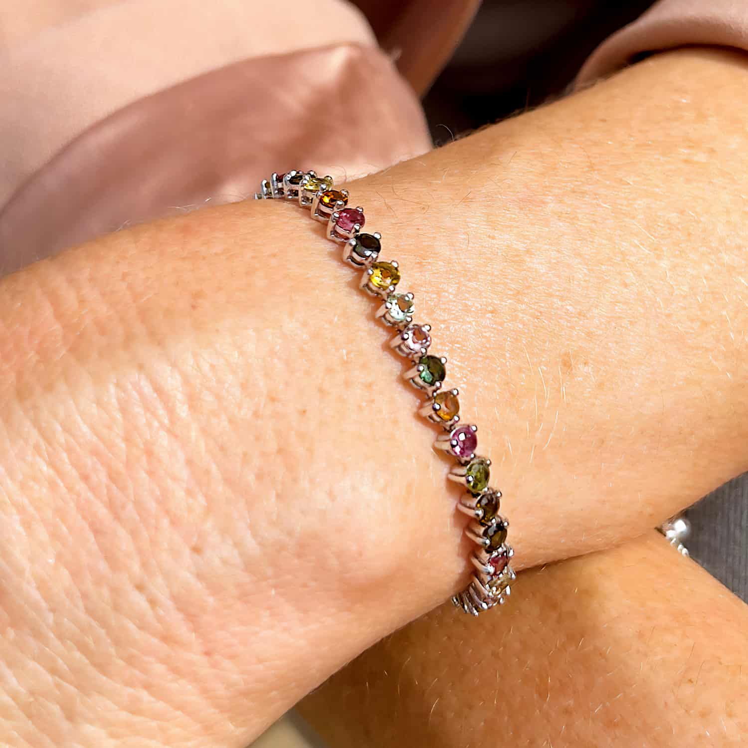 Sterling Silver Tennis Bracelet with 30 Round Brilliant Cut Multicoloured Tourmaline gemstones, seen slightly from the top and side on a woman's wrist.