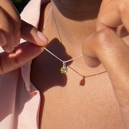 Woman holding up Peridot Pendant necklace. 5mm round Peridot gemstone in four claws on 45cm curb chain."