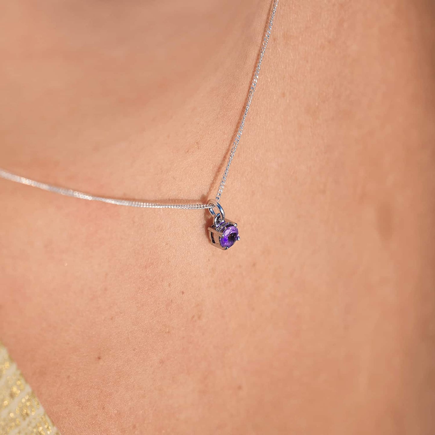 Close-up of a woman wearing the Amethyst Pendant necklace, highlighting a 5mm round Amethyst gemstone set in four claws on a 45cm sterling silver curb chain.