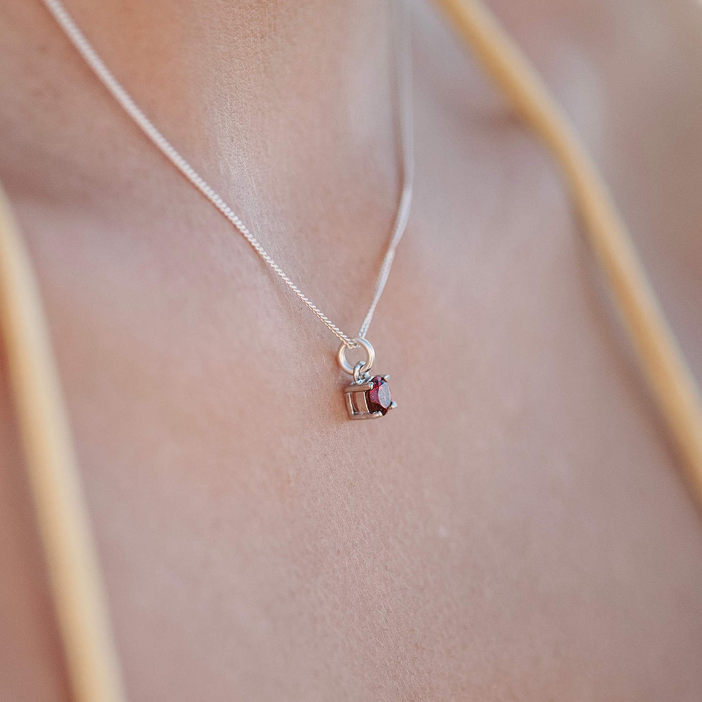 Close-up side view of woman wearing the Garnet Pendant necklace. The necklace features a 5mm round Garnet gemstone set in four claws on a 45cm curb chain.