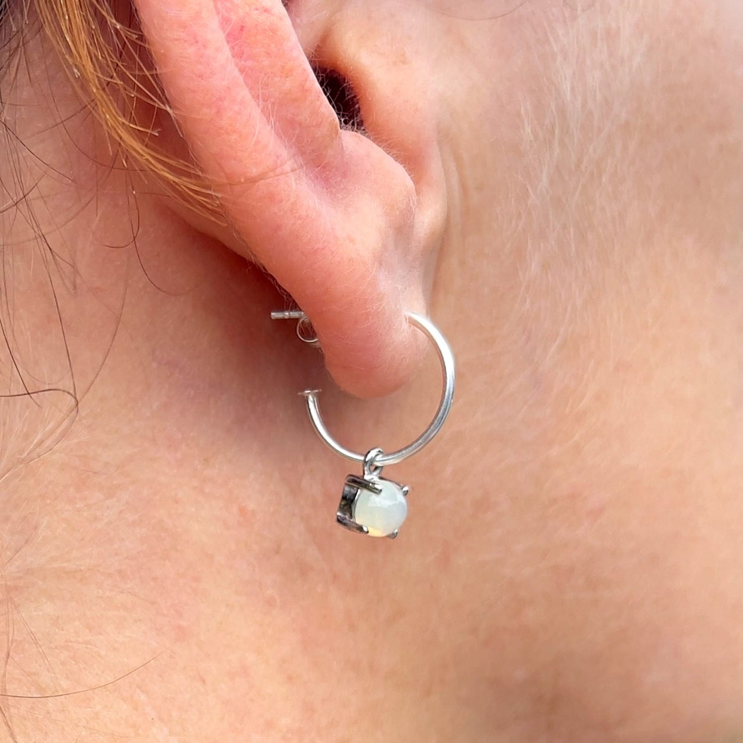 Woman's ear with slight side view featuring Ethiopian Opal Dangle Hoop earring, showcasing stunning opal gemstone.