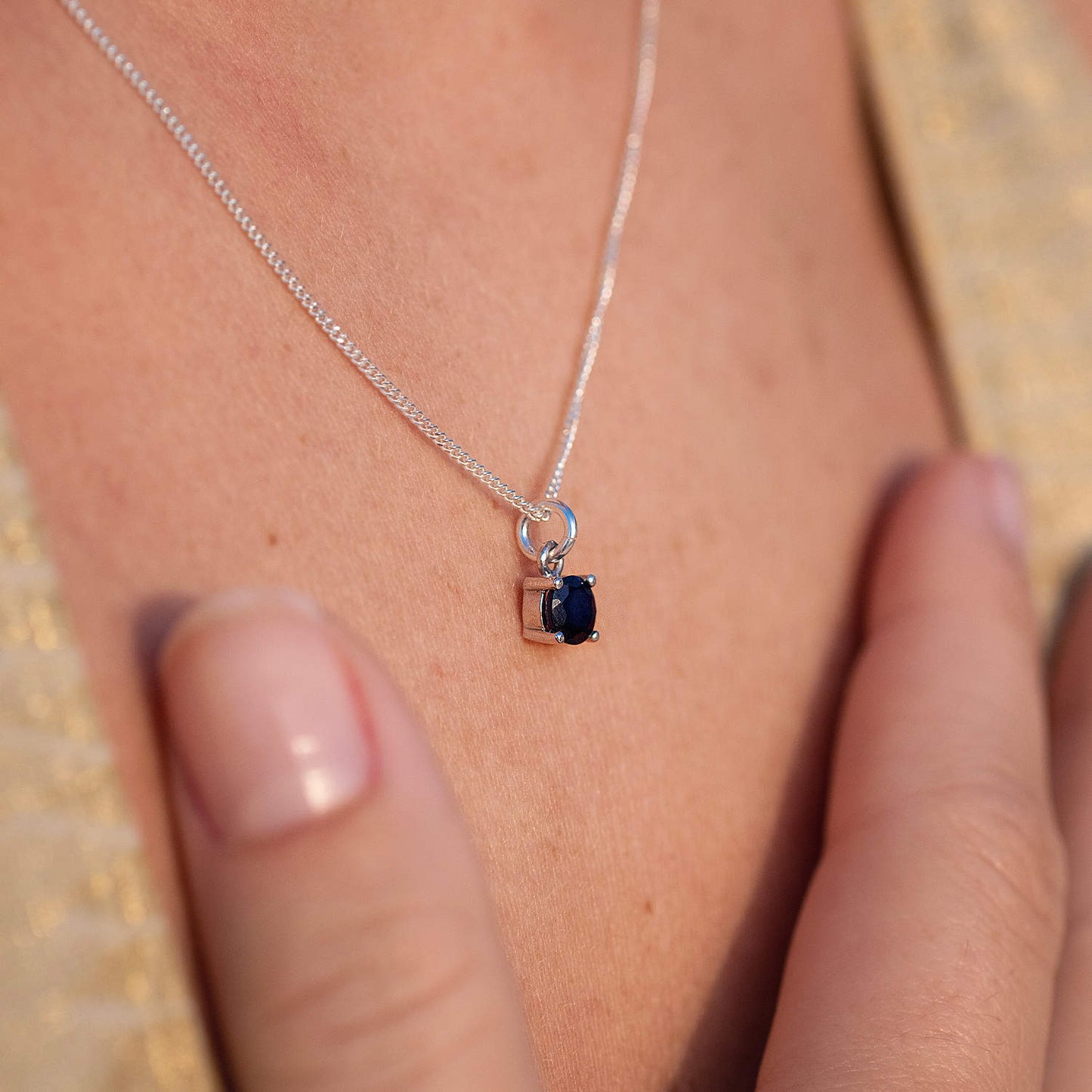 Woman wearing Sapphire Pendant necklace, close-up side view. 5mm round Sapphire gemstone set in four claws on 45cm curb chain.