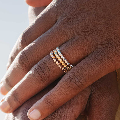 Close up of a Sterling Silver heart-shaped ring with multiple interlocking hearts forming a band in silver, yellow gold, and rose gold on a woman's hands