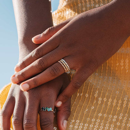 A Sterling Silver heart-shaped ring with multiple interlocking hearts forming a band in silver, yellow gold, and rose gold on a woman's hands