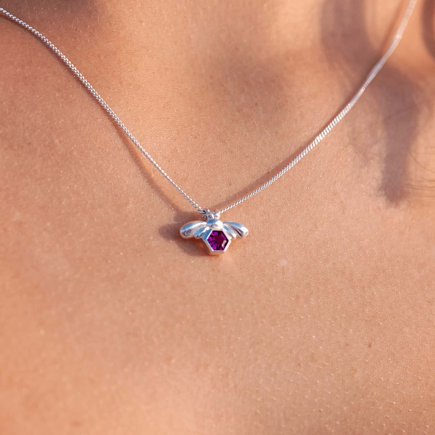 Close-up image of a woman wearing the Bee-YOU-tiful Bee Pink Tourmaline Bling, showcasing a 45cm curb chain and a Sterling Silver pendant featuring a bee and a 4mm hexagonal Pink Tourmaline gem set in its belly with a tube setting.